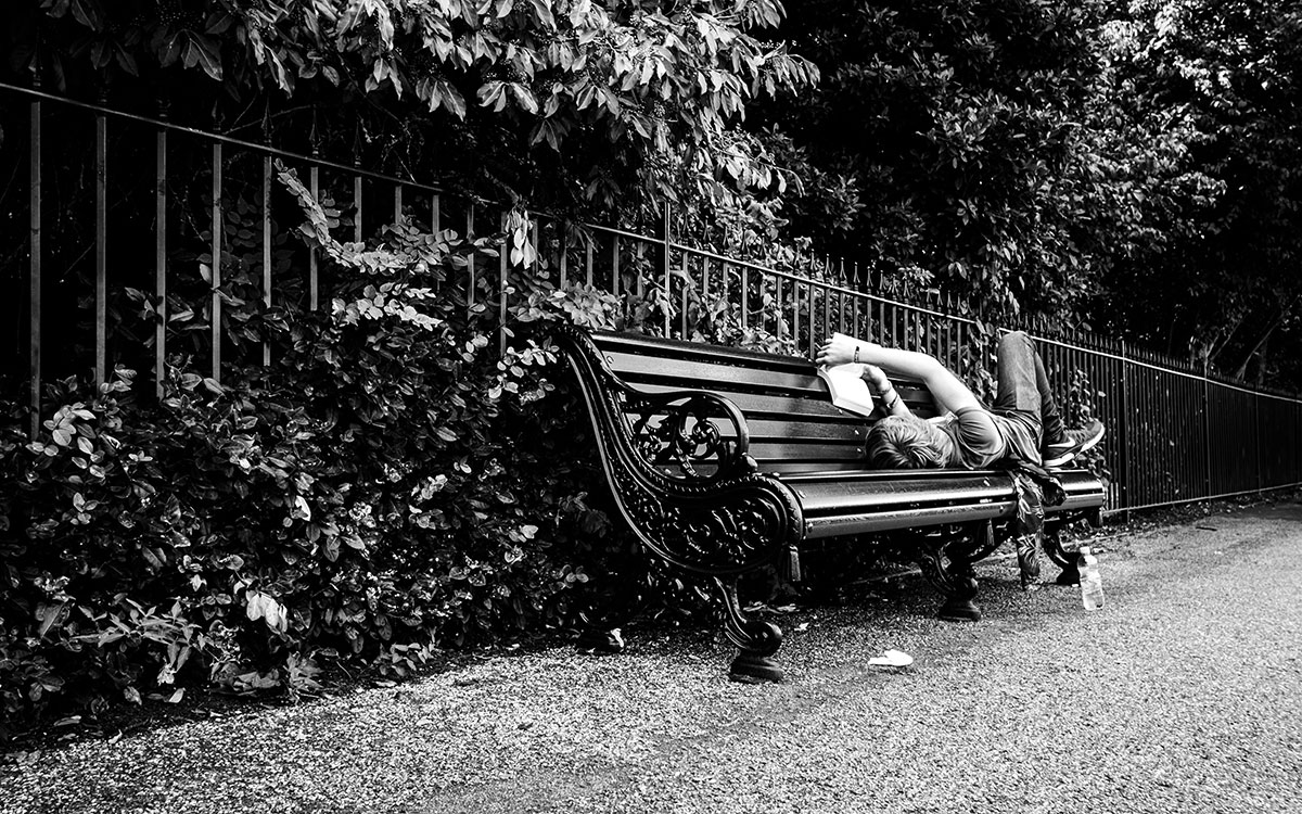 Manb beim Buch lesen liegend auf einer Parkbank